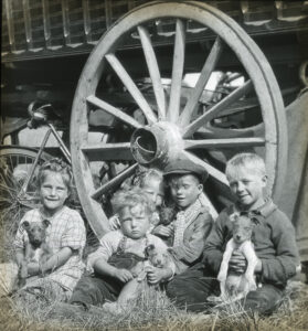 Historic photograph of travelling families gathered beneath a large wagon wheel